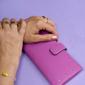 Magenta wallet held by two hands on a purple background - MAGENTA