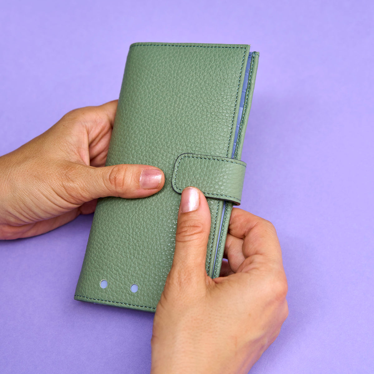 Green wallet held by hands against a purple background - SAGE