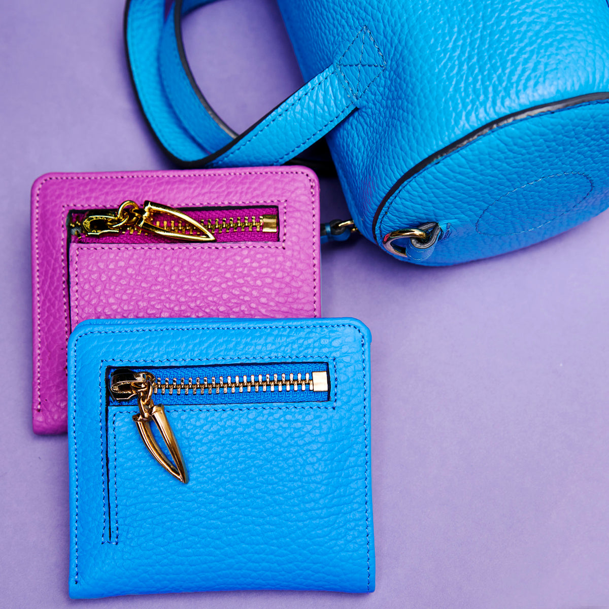 Two blue and magenta leather wallets with gold zippers on a purple background - AZURE