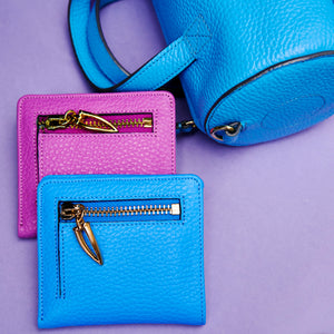 Two blue and magenta leather wallets with gold zippers on a purple background - AZURE