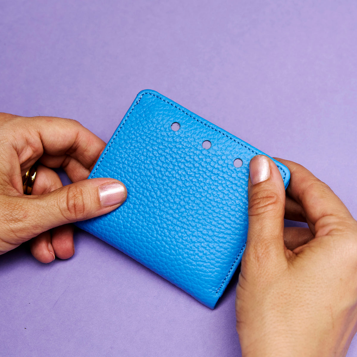 Blue textured wallet held by hands against a purple background - AZURE