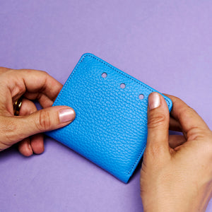Blue textured wallet held by hands against a purple background - AZURE