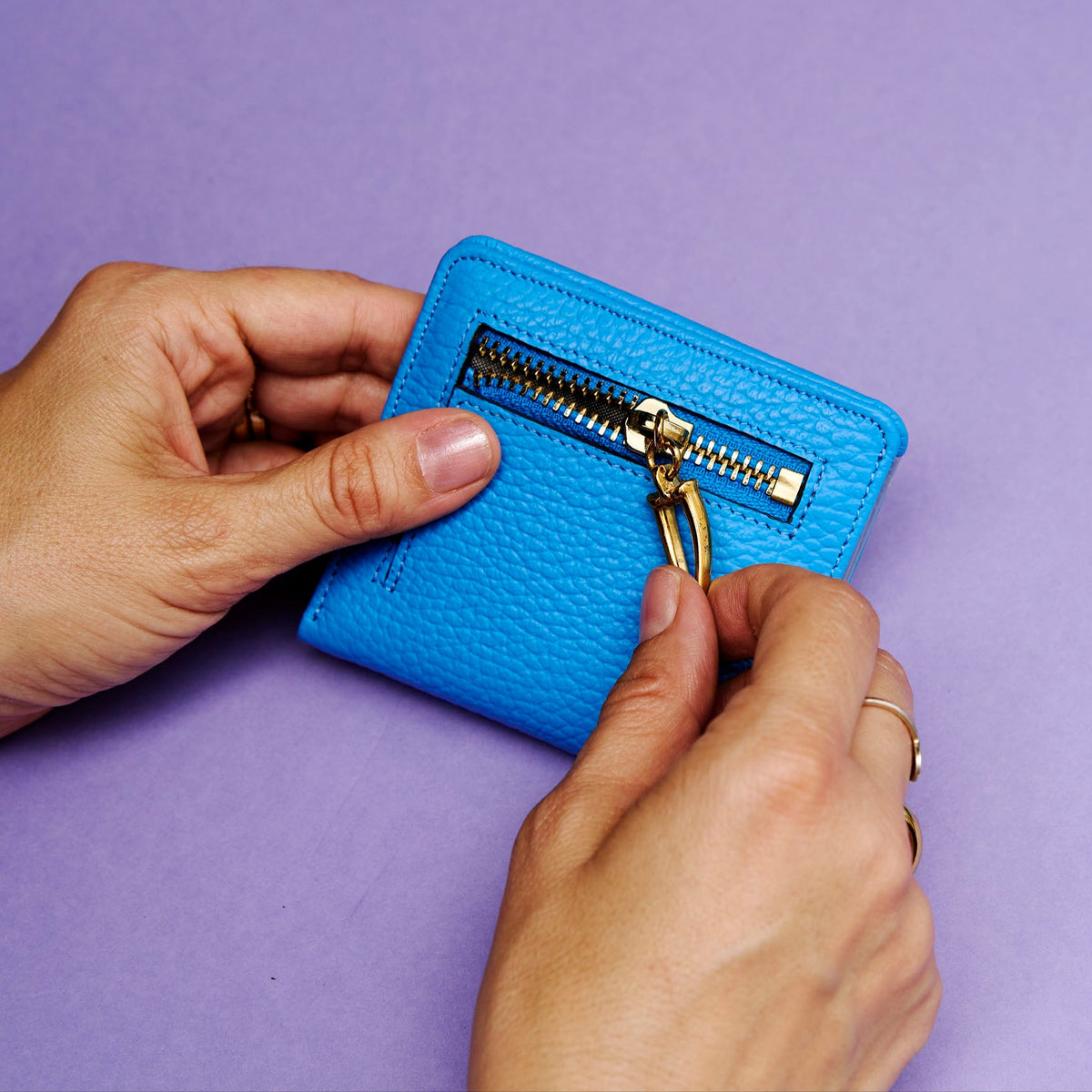 Blue wallet with gold zipper being held against a purple background - AZURE