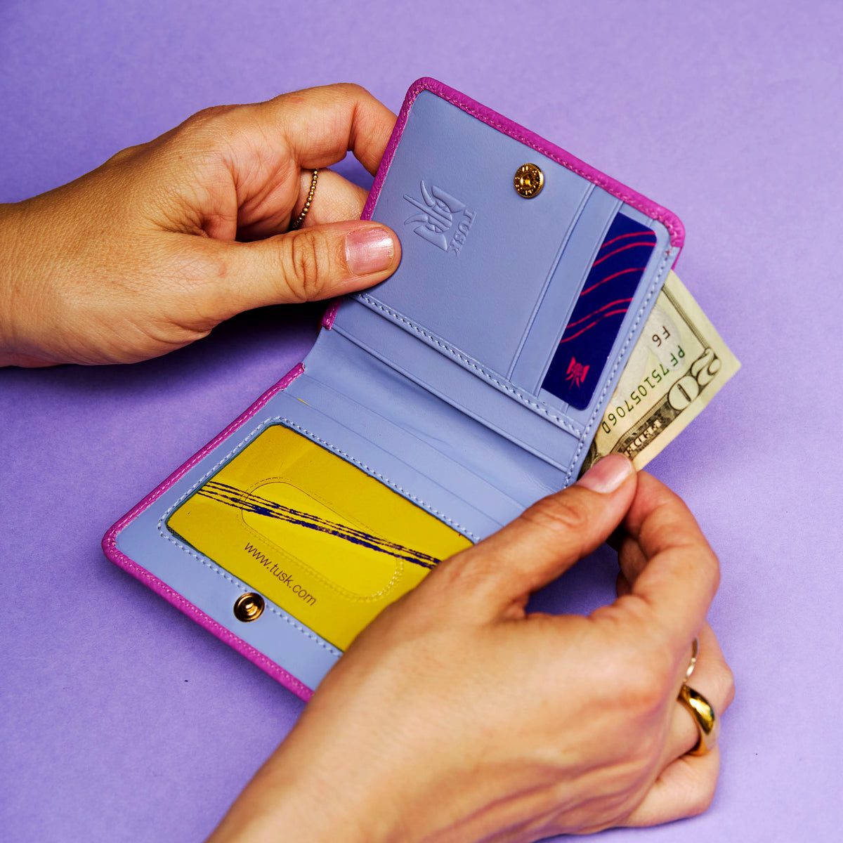 Person holding an open magenta leather wallet with blue interior against a purple background - MAGENTA