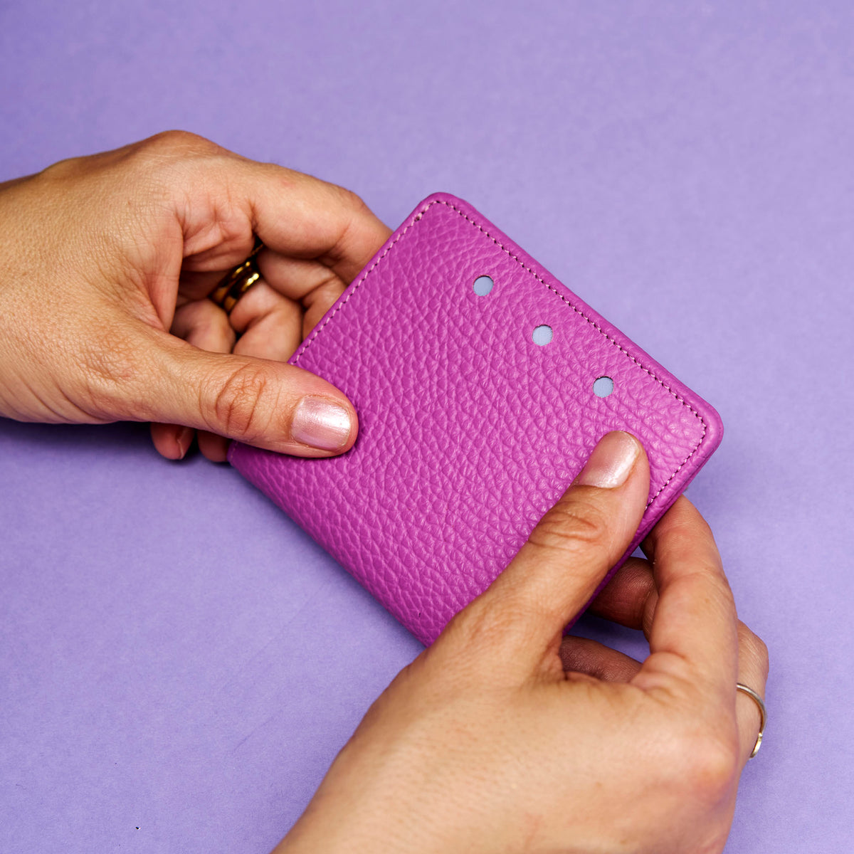 Magenta leather wallet held by hands against a purple background - MAGENTA