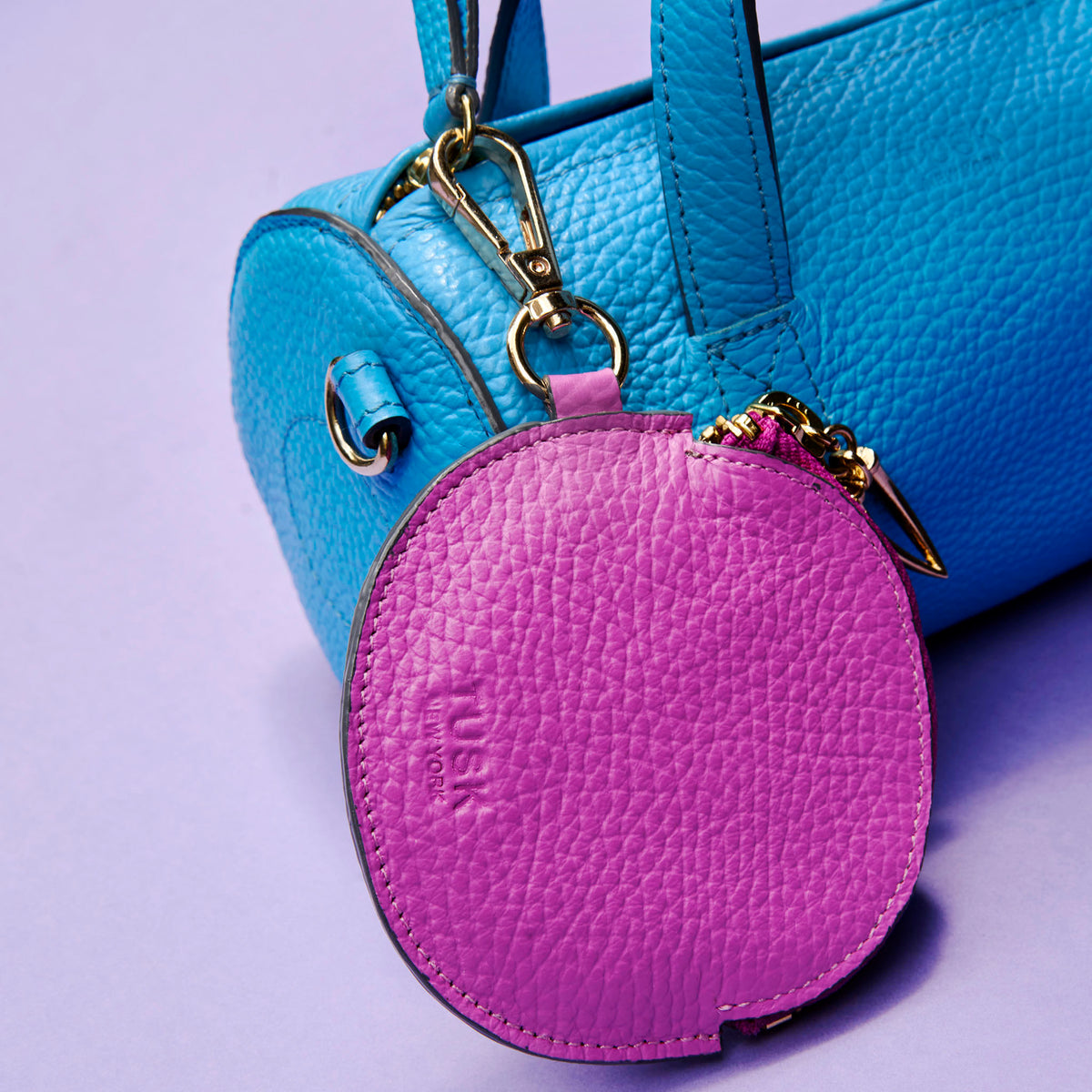Purple leather coin purse charm attached to a blue leather barrel bag on a light purple background - MAGENTA