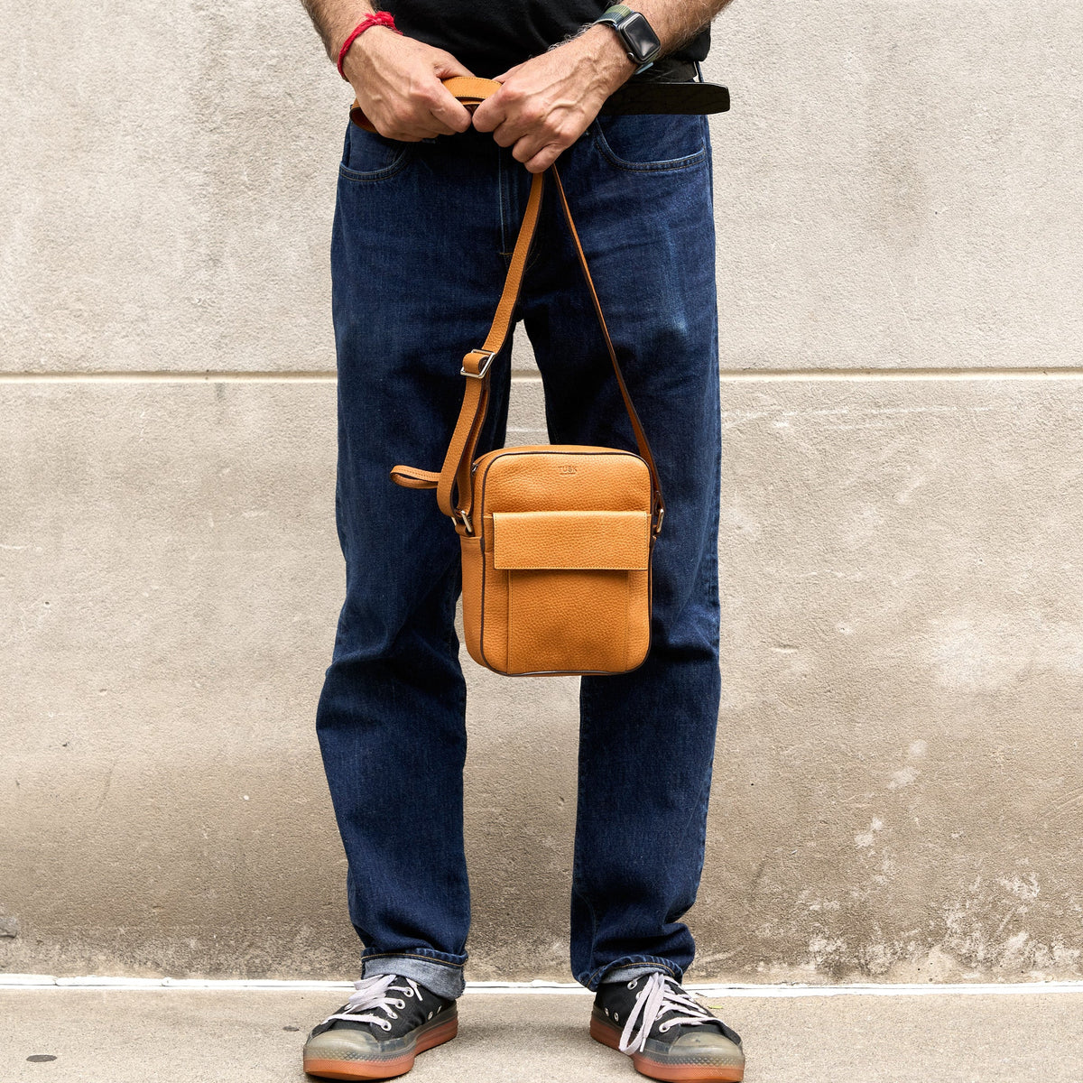 Person holding a brown leather bag against a concrete wall