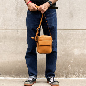 Person holding a brown leather bag against a concrete wall