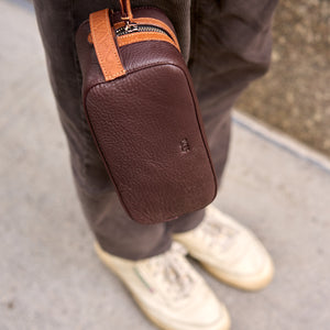 Brown leather toiletry bag with tan accents worn by a person on a sidewalk - CHOCOLATE