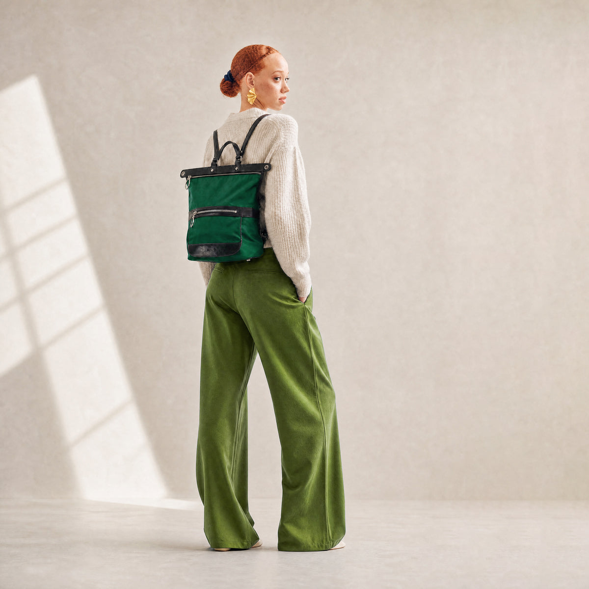 Person wearing a green backpack and green pants in a minimalistic setting - FOREST