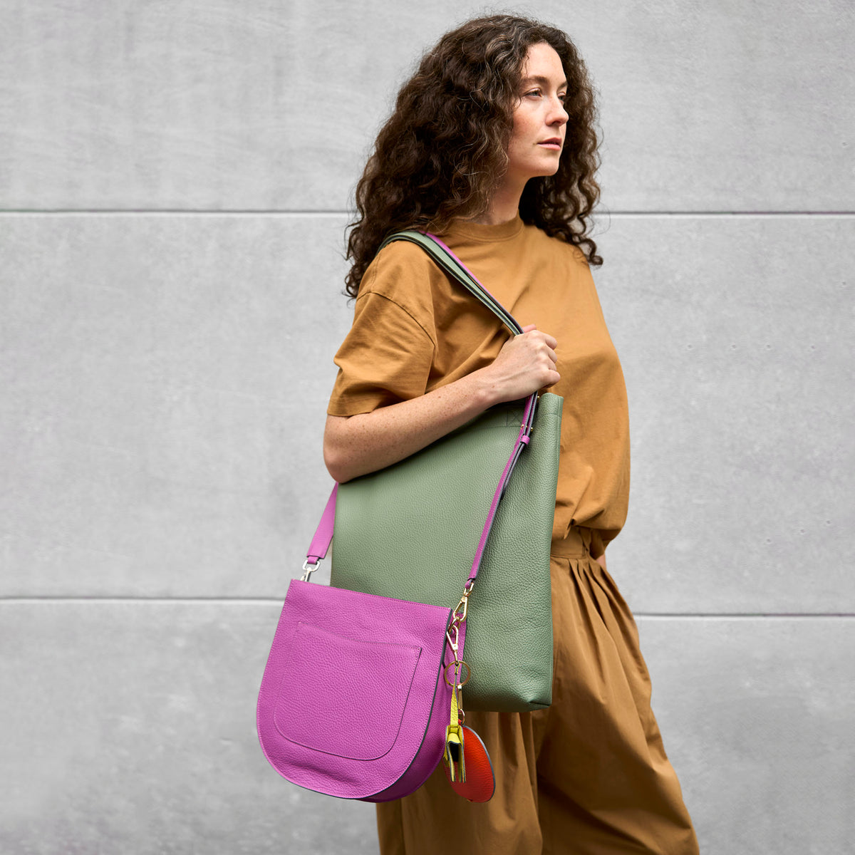 Woman holding a green and magenta bag against a gray wall - MAGENTA