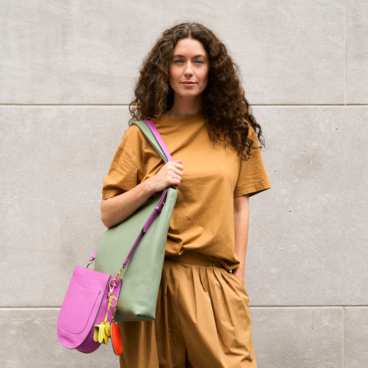 Woman holding a 2 colorful handbags against a gray wall - MAGENTA