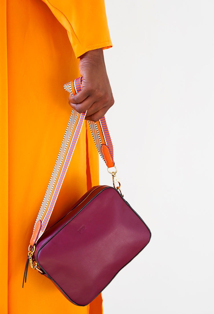 A woman in an orange dress carrying a maroon shoulder bag with a striped strap.