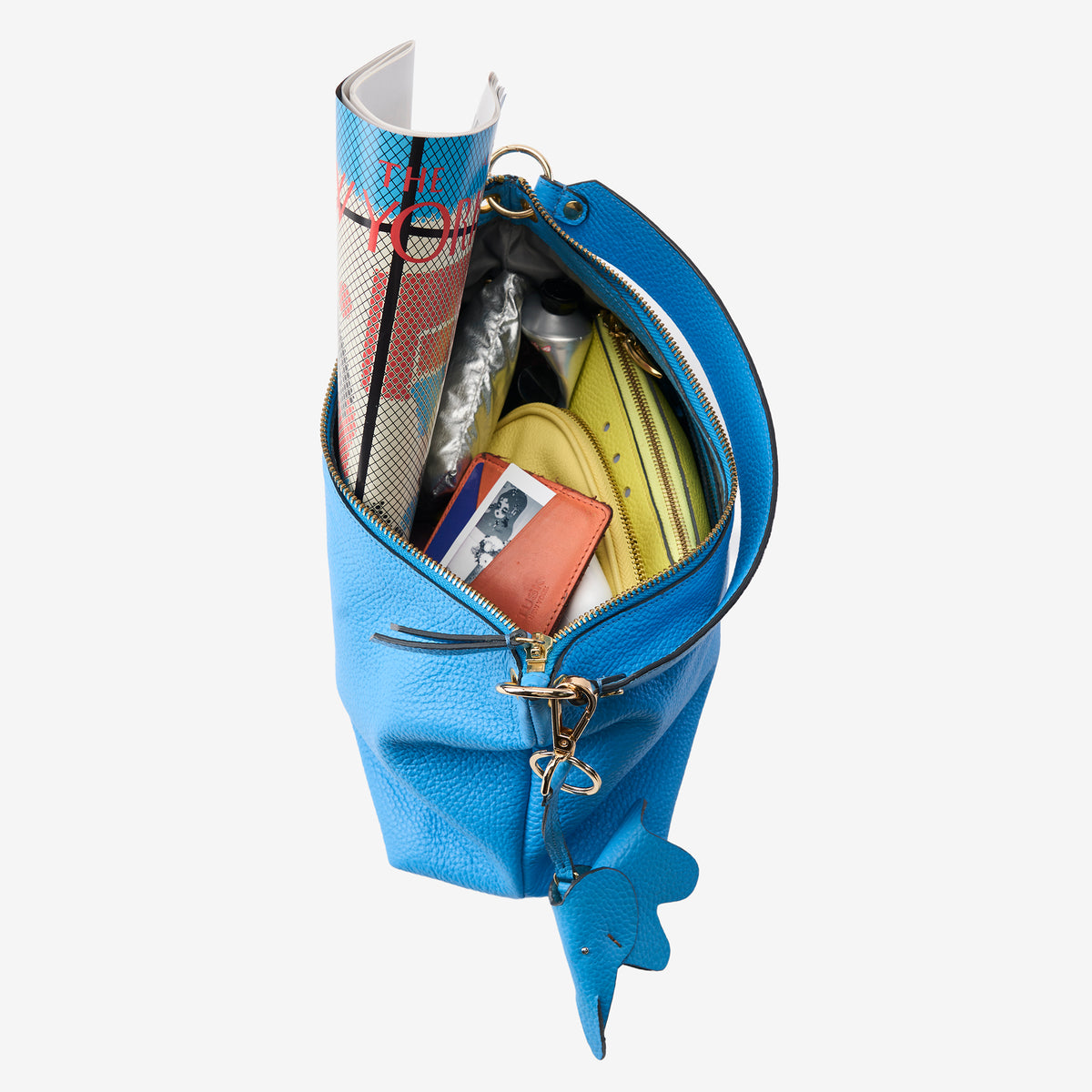 Top-down view of a bright azure blue pebbled leather tote bag with gold hardware and zip closure, styled open to reveal everyday essentials including a magazine, yellow zip pouch, small leather card case and silver pouch - AZURE