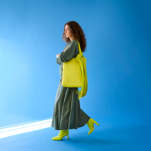 Woman holding a bright yellow leather tote bag against a blue background - LIME