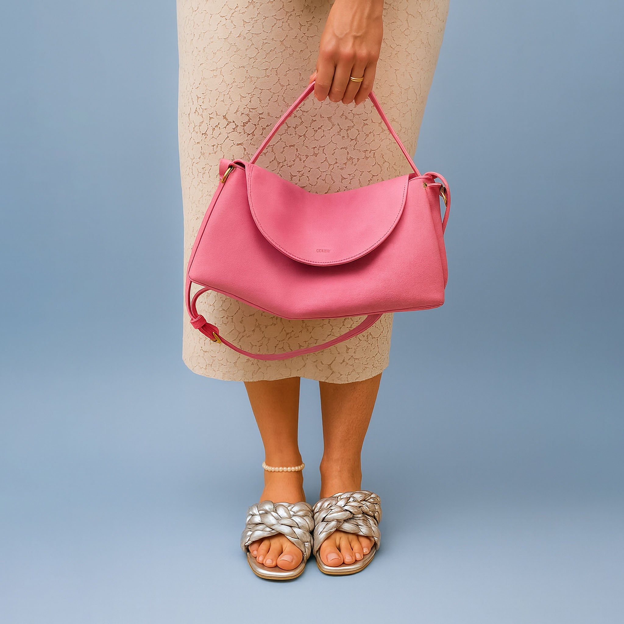 Person holding a pink suede handbag against a plain background - BLUSH