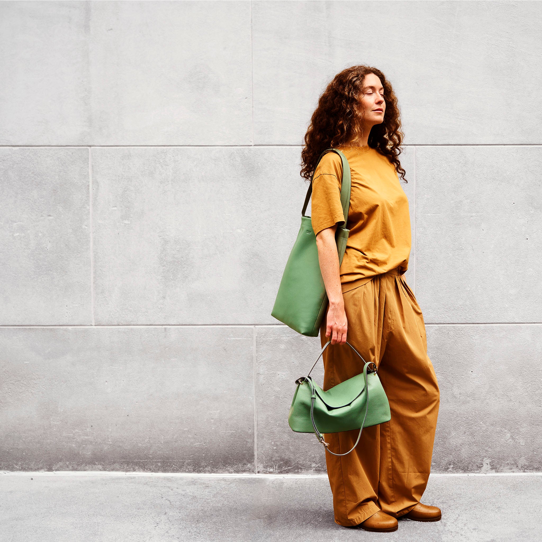 Woman holding a green italian leather handbag against a gray wall - SAGE