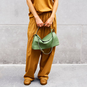 Person holding a green handbag against a gray background - SAGE