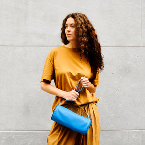 Woman holding a blue handbag against a gray wall - AZURE
