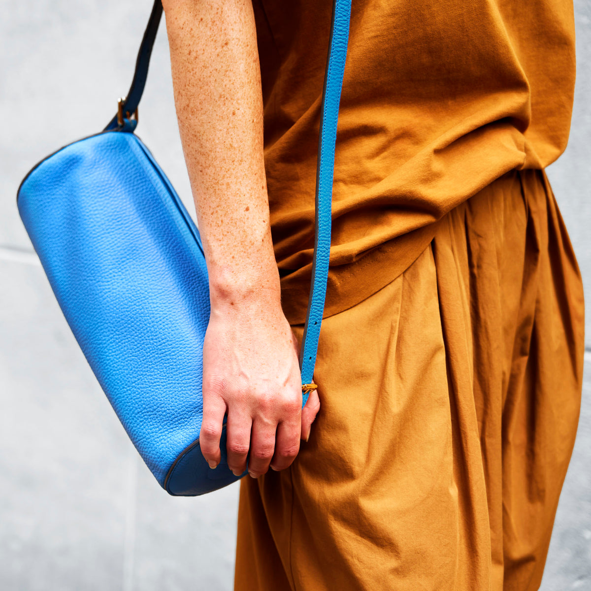 Person holding a blue leather  barrel bag with a plain background - AZURE