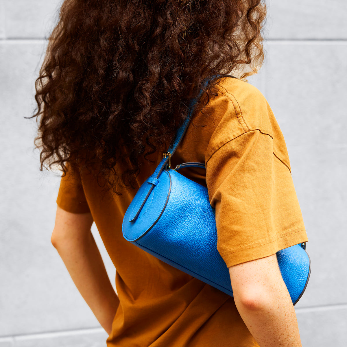 Person wearing a mustard yellow shirt with a blue handbag over their shoulder against a light gray background - AZURE