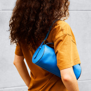Person wearing a mustard yellow shirt with a blue handbag over their shoulder against a light gray background - AZURE