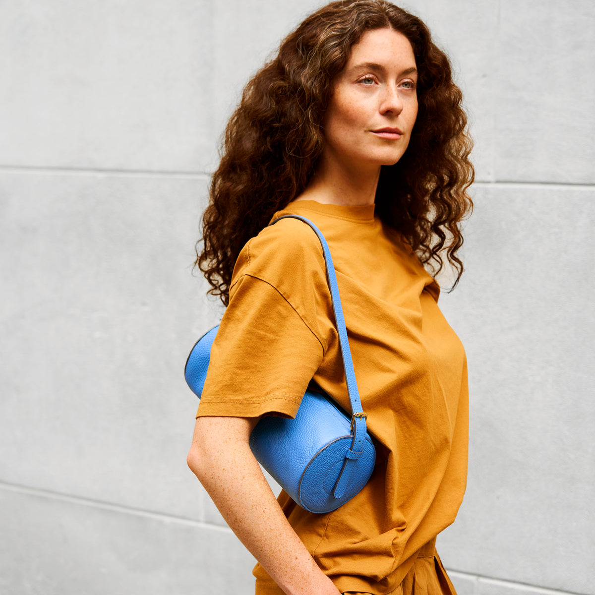Woman carrying a blue leather handbag against a gray wall - AZURE