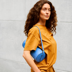 Woman carrying a blue leather handbag against a gray wall - AZURE