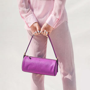 Person wearing light pink outfit holding a magenta round leather bag against a white wall -MAGENTA