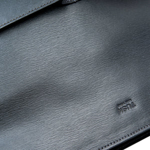 Close-up of a dark gray textured leather bag with visible grain and a small debossed logo near the lower right.