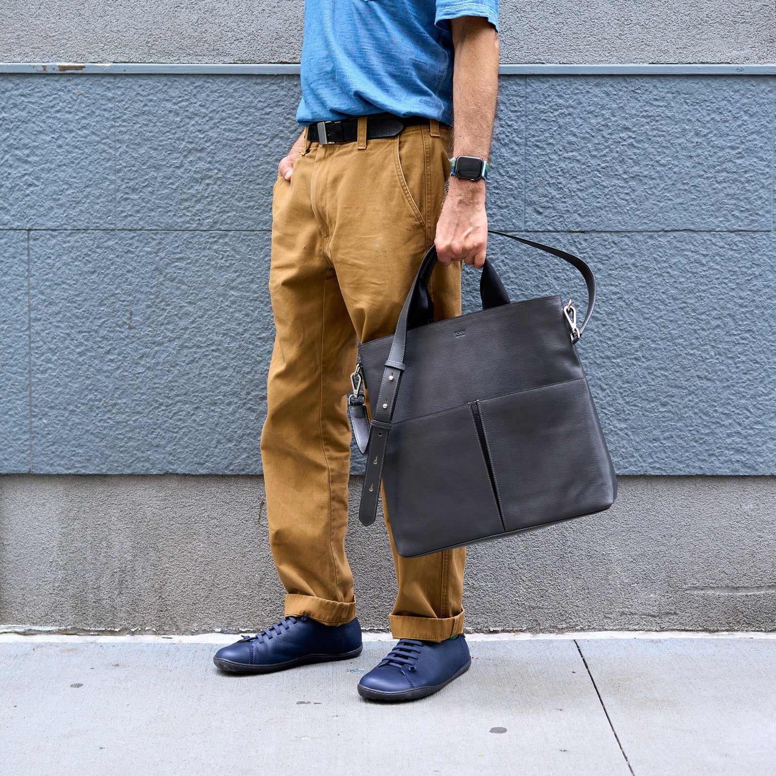 A dark gray leather tote bag with two top handles, a top zipper closure, and two large front slip pockets, shown against a plain white background - CHARCOAL