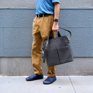 Person holding a gray leather bag against a gray wall - CHARCOAL
