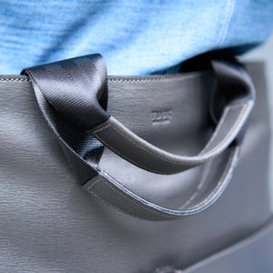 Close-up of a gray handbag with a black ribbon handle - CHARCOAL