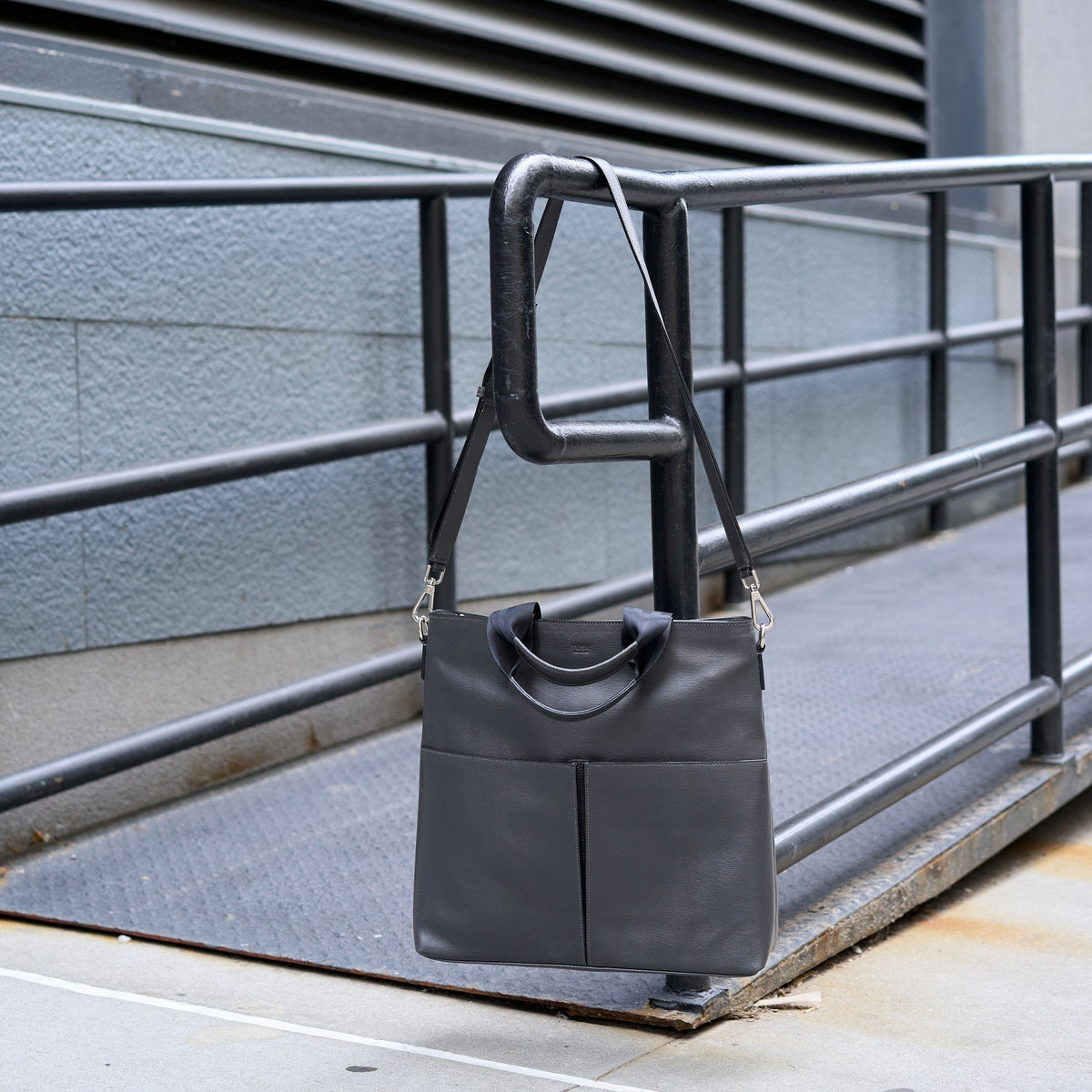 Gray leather handbag hanging on a metal railing outdoors - CHARCOAL