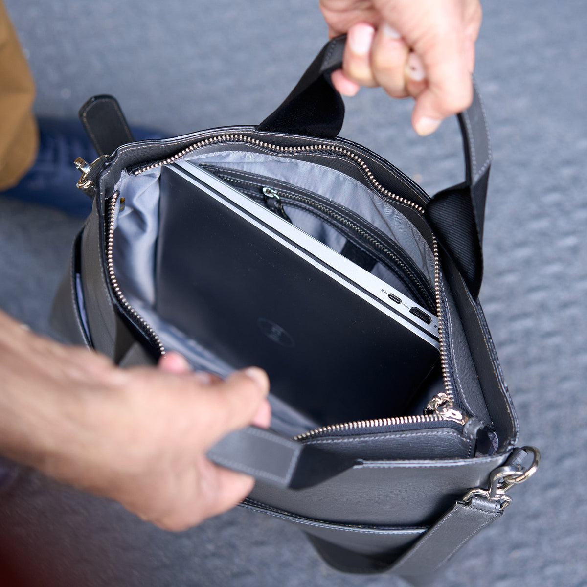 Person opening a gray leather bag to reveal a laptop inside - CHARCOAL