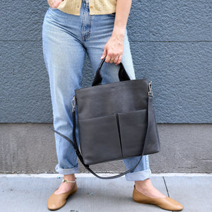 Woman holding a grey leather tote against a gray wall - CHARCOAL
