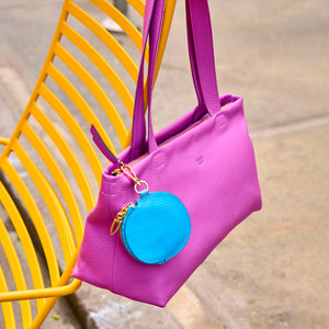 Purple handbag with a blue round keychain on a yellow chair - MAGENTA