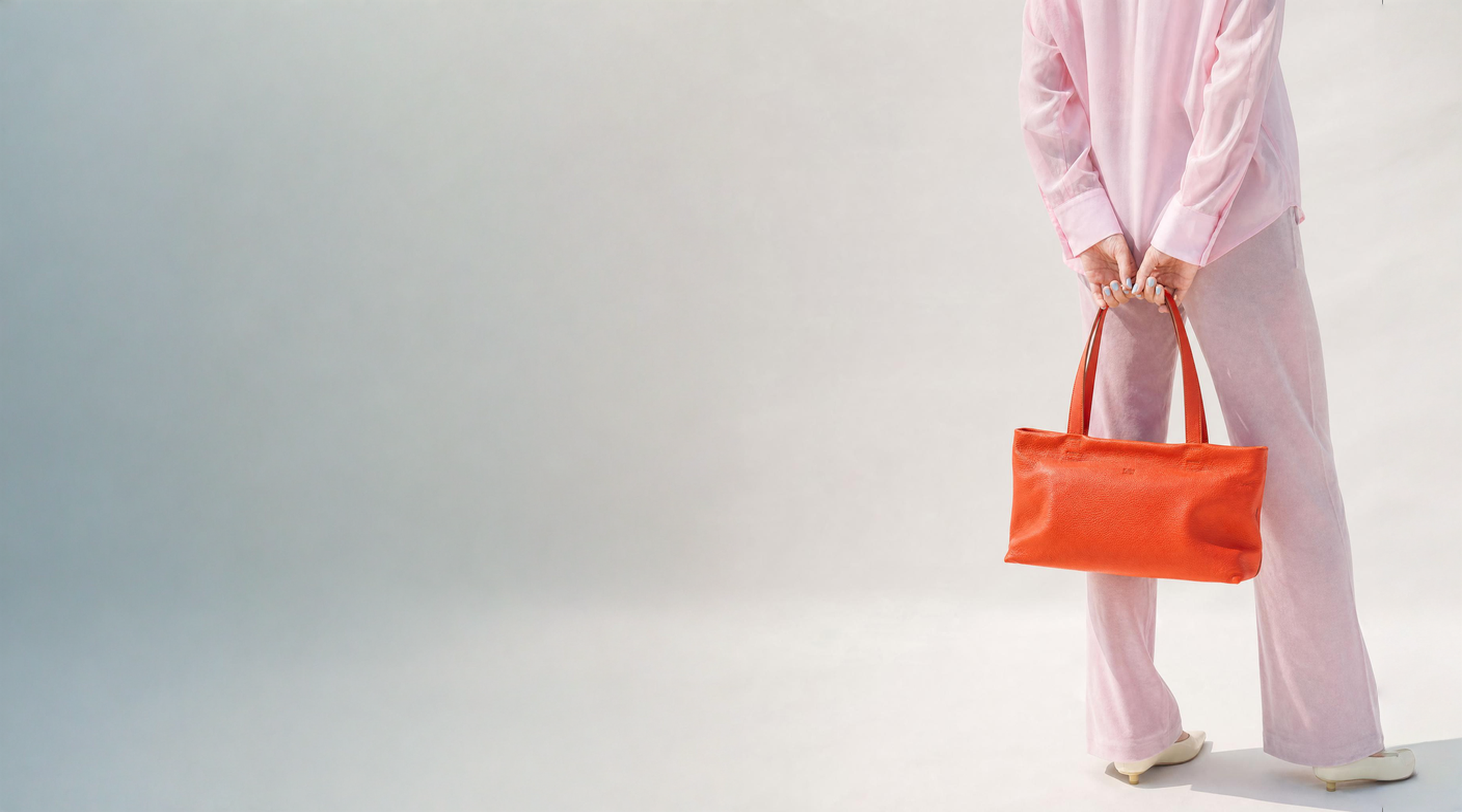 Person holding an orange tote bag against a light gray background