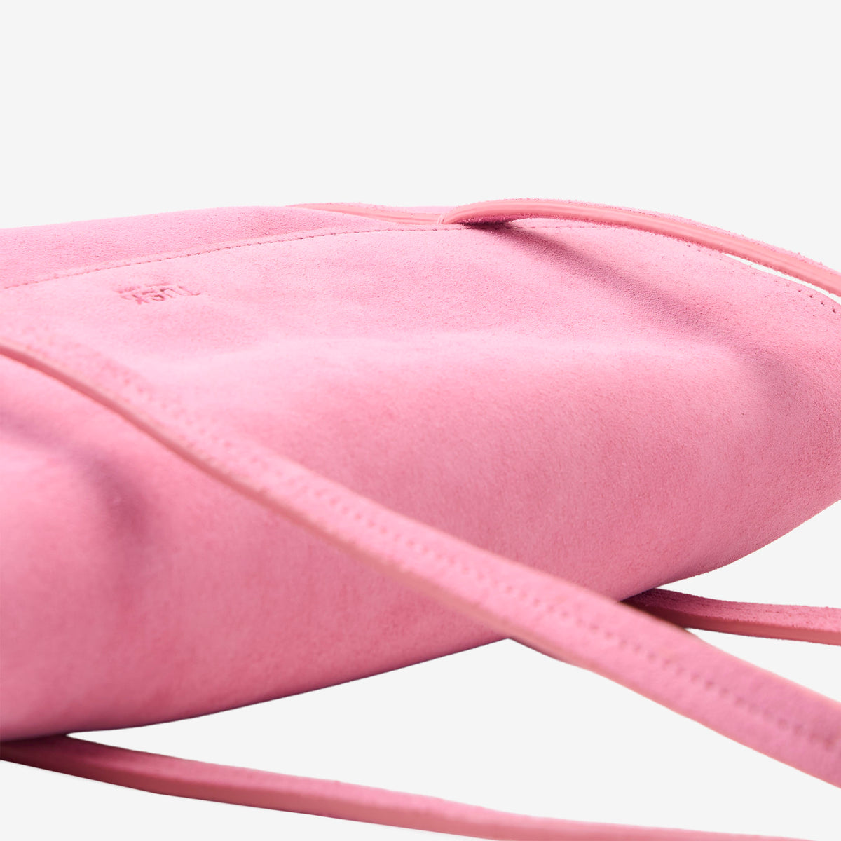 Close-up detail view of the blush pink Italian suede Vienatta | Jyoti shoulder bag, highlighting its soft suede texture, fine edge stitching, thin double shoulder straps, and the subtle embossed Tusk logo on the top flap against a plain light gray background - BLUSH