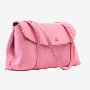 Three-quarter profile view of the blush pink Italian suede Vienatta | Jyoti shoulder bag, showcasing its softly structured side silhouette, stitched flap closure with the Tusk logo stamped on the front, and thin double shoulder straps against a plain light gray background - BLUSH