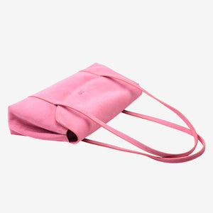 High-angle view looking down into the open blush pink Italian suede Vienatta | Jyoti shoulder bag, revealing its main interior compartment, envelope flap, stamped Tusk logo, and thin double shoulder straps laid to the right on a plain light gray background - BLUSH