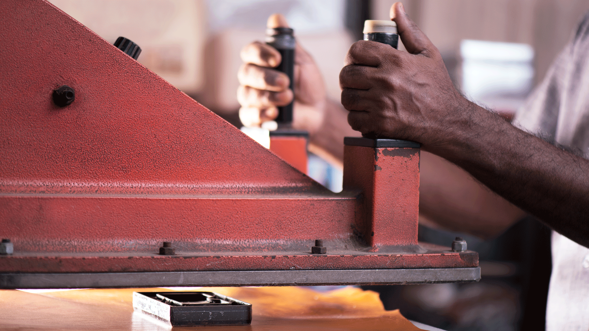 Worker's hands operating a red industrial machine in a workshop setting.