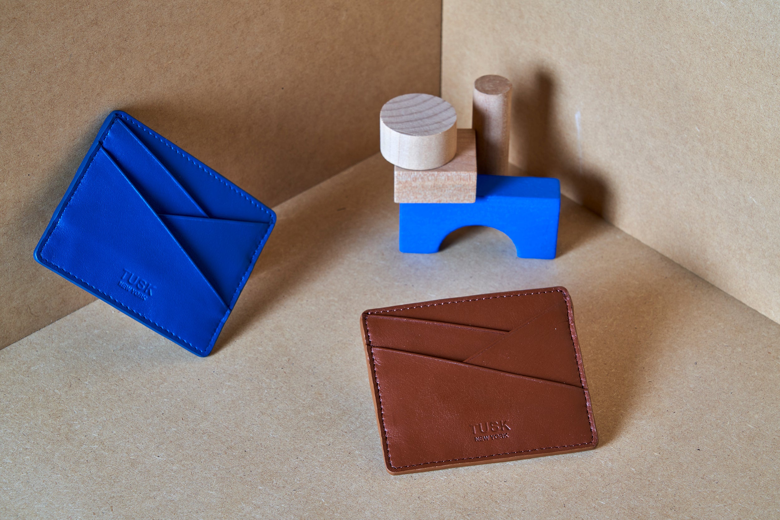 Blue and brown leather wallets displayed with wooden blocks on a craft paper background