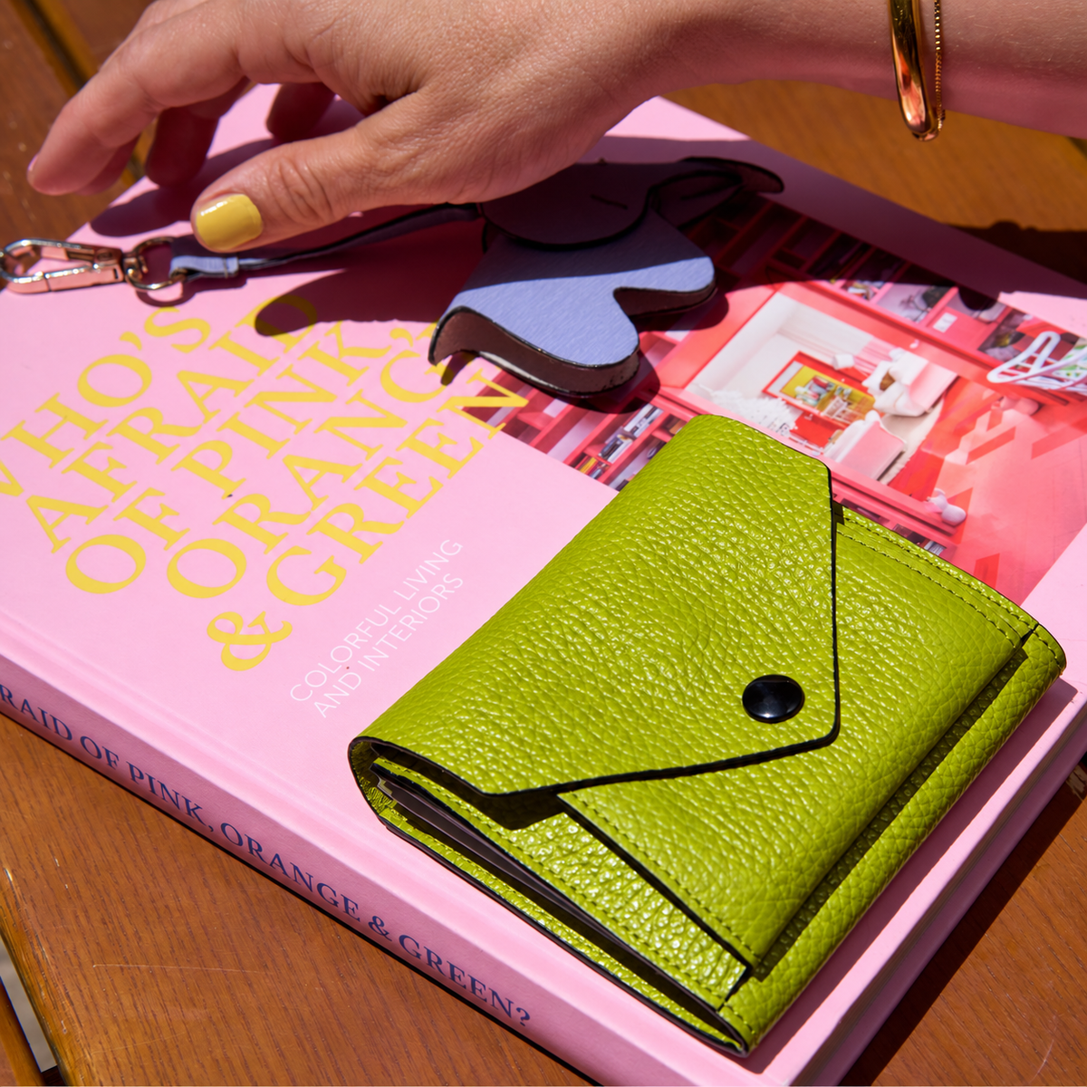 Tusk 382 Ascot Origami Wallet in avocado Italian pebble-grain cowhide leather. Closed wallet lifestyle view on a pink book, showing matching stitching and pebble-grain leather - AVOCADO