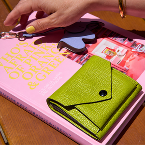 Tusk 382 Ascot Origami Wallet in avocado Italian pebble-grain cowhide leather. Closed wallet lifestyle view on a pink book, showing matching stitching and pebble-grain leather - AVOCADO