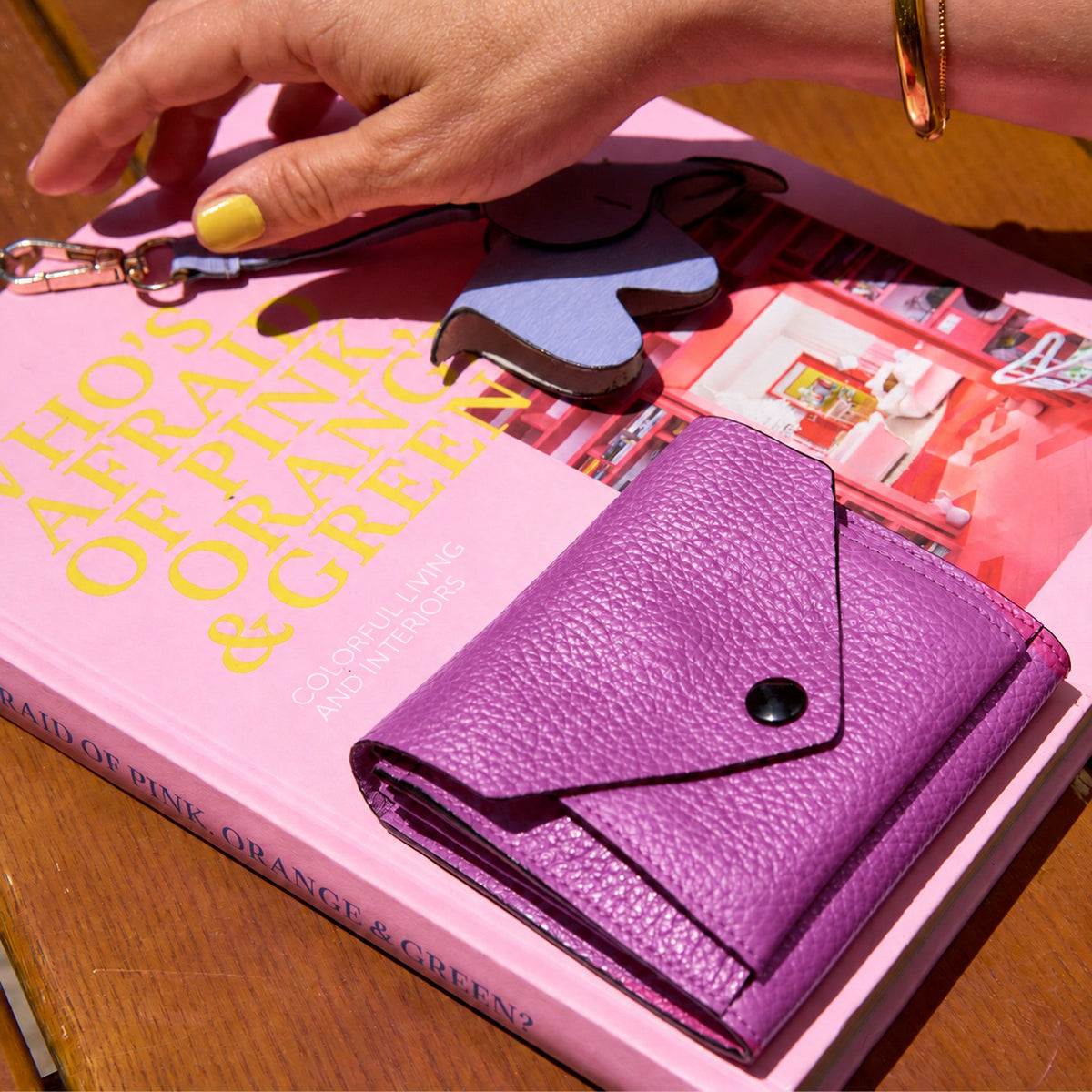 Tusk 382 Ascot Origami Wallet in magenta Italian pebble-grain cowhide leather. Closed wallet lifestyle view on a pink book, showing matching stitching and pebble-grain leather - MAGENTA