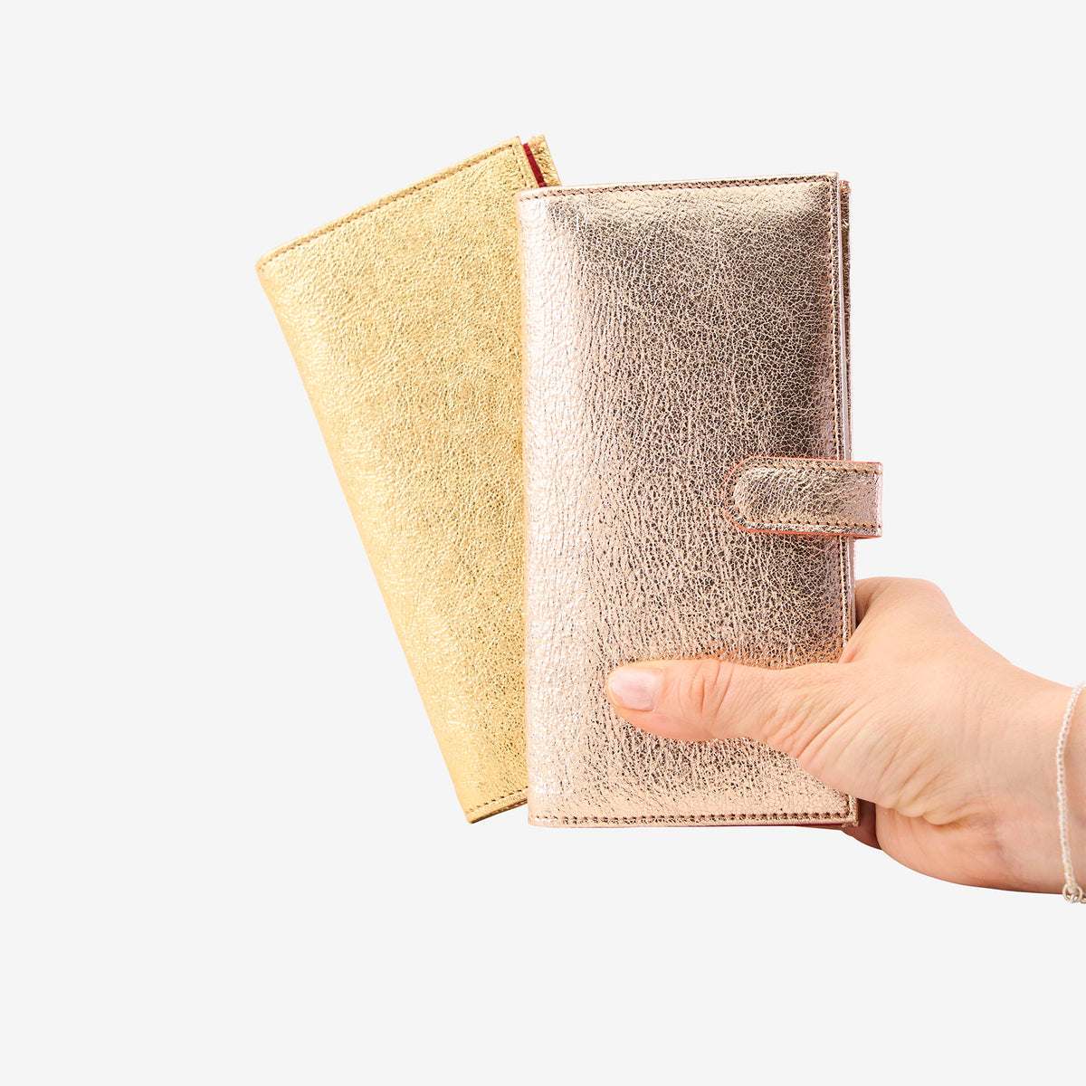 Hand holding two metallic leather wallets, one gold and one rose gold, on a white background - GOLD