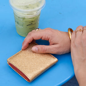 Gold metallic leather wallet and green iced drink on a blue surface - GOLD