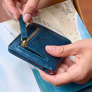 Blue metallic leather wallet with gold zipper held by hands on top of a book - NAVY