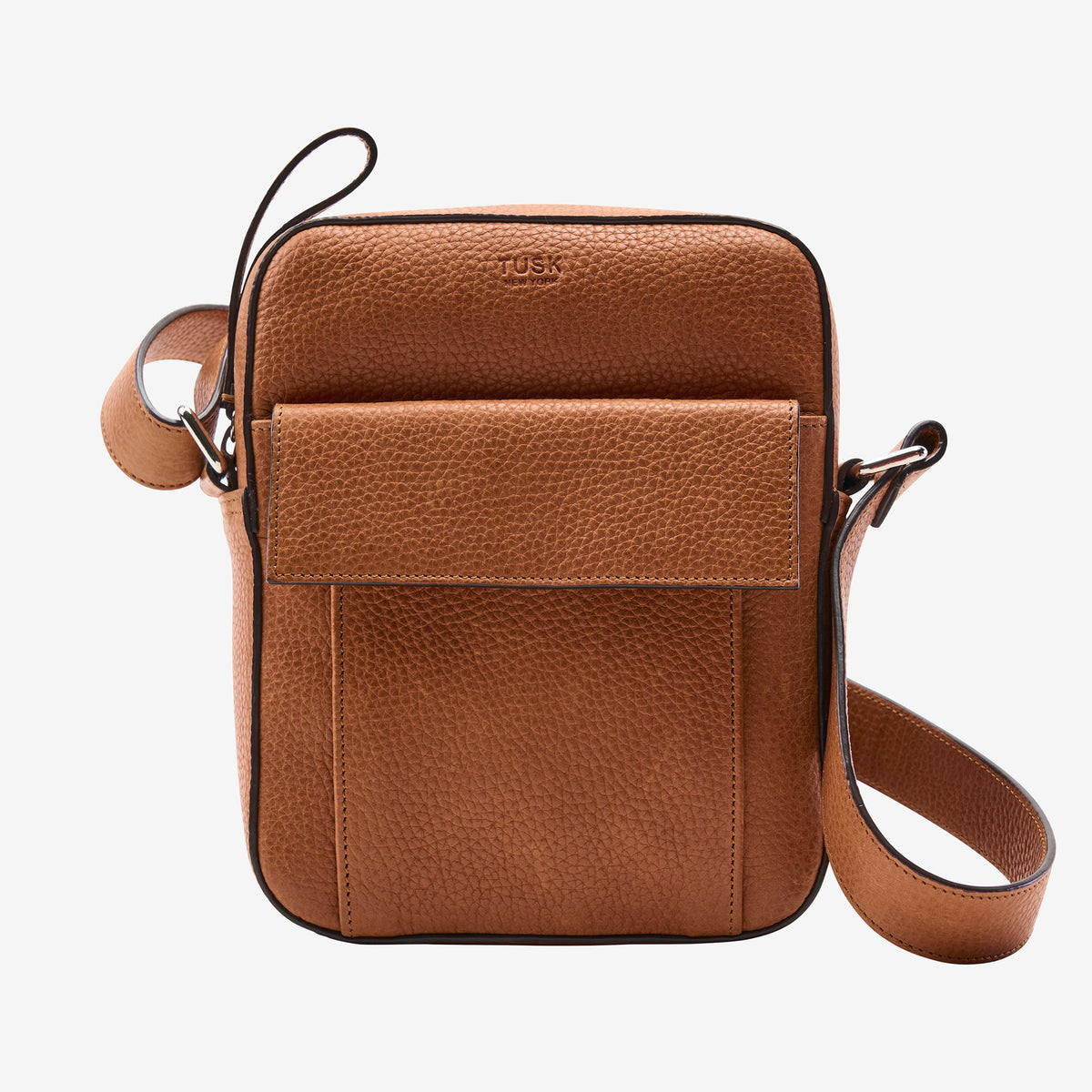 A tan pebbled leather crossbody bag with a front flap pocket and a matching adjustable shoulder strap, shown on a light gray background. The brand name 'TUSK' is subtly embossed on the top front - TOAST